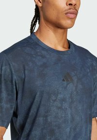 Camiseta deportiva de color azul marino con un diseño texturizado y el logo negro de Adidas en el pecho. Mangas cortas y escote redondo.