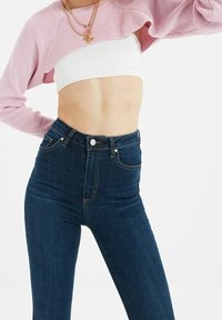 Suéter corto rosa con textura de canalé; parte superior blanca ajustada por debajo. Jeans skinny de cintura alta en azul oscuro con bolsillos frontales y costuras en contraste.