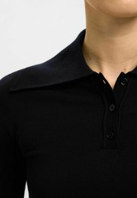 Černá polo košile s dlouhým rukávem a límcem, která má řadu tří knoflíků, ribbovanou texturu a přiléhavý design.