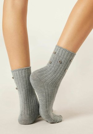 Chaussettes grises à côtes avec des accents métalliques décoratifs le long de la manchette, offrant un ajustement moulant et une texture douce.