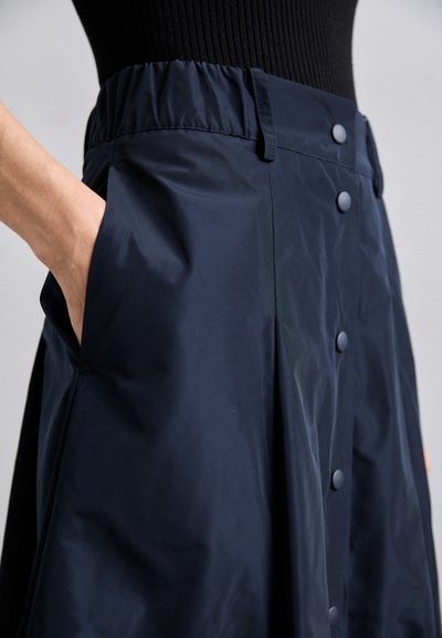 Jupe légère bleu marine avec une texture lisse, taille élastique, poches latérales et détails de boutons sur le devant.