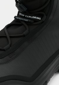 Černá turistická bota s texturovaným svrškem, gumovou podrážkou, elastickými tkaničkami a viditelnou štítkem s nápisem "The North Face".