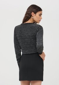 Maglione nero a trama con maniche lunghe, caratterizzato da un colletto a coste. Il modello indossa una gonna nera aderente, mostrano una vista di profilo laterale.