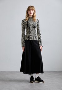 Top a maniche lunghe a righe bianche e nere abbinato a una gonna nera plissettata e sneakers nere, con calzini bianchi e dettagli dorati.