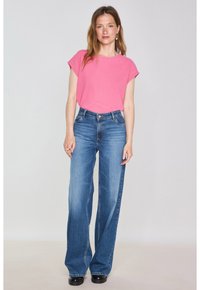 T-shirt rosa a maniche corte abbinato a jeans blu a vita alta e gamba larga. L'outfit presenta una vestibilità casual e una texture di tessuto liscia.