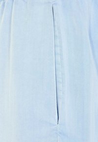 Tissu en coton bleu clair avec une couture visible et une fente sur le côté. La texture est lisse avec un léger éclat. Design simple et épuré.