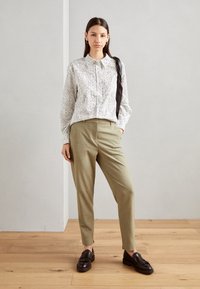 Balta marškinėliai su juodais taškeliais, khaki spalvos siauri džinsai ir tamsiai rudos spalvos loafers su fringu. Minimalistinis dizainas, lygus paviršius.