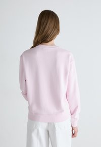 Light pink sweatshirt with a crew neck, ribbed cuffs, and hem. Fabric appears soft and slightly textured, designed for a relaxed fit.