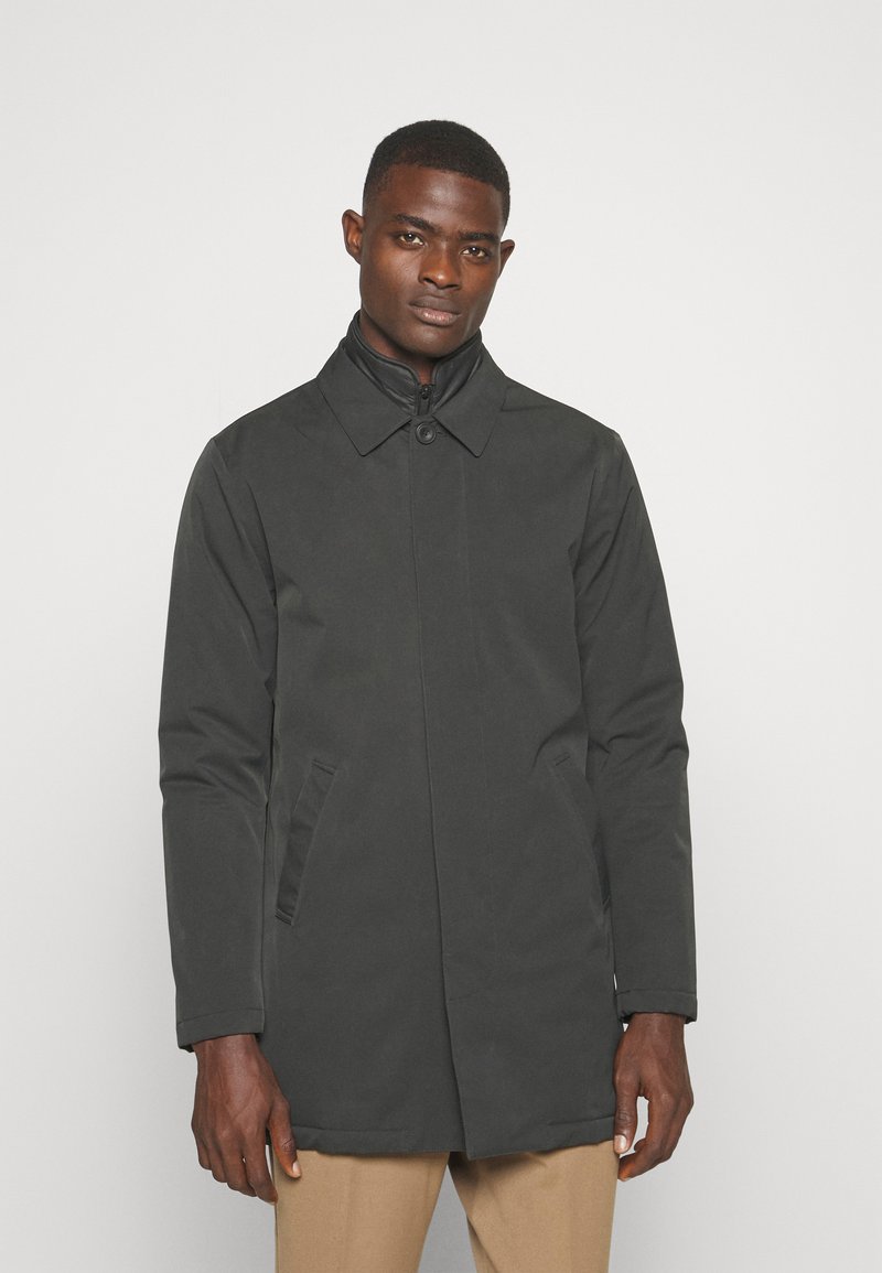 Abrigo negro impermeable con cuello, cierre de cremallera y botones, dos bolsillos laterales y una textura exterior suave. La longitud llega a la mitad del muslo.