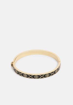 Bracelet jonc doré avec émail noir présentant des logos ronds répétés et une fermeture à boucle, présenté sur un fond clair uni.