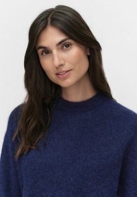 Granatowy sweter wełniany z okrągłym dekoltem i miękkim, teksturowanym wykończeniem. Długie rękawy i luźny krój.