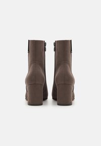 Bottes marron en suédine synthétique à cheville avec un talon bloc haut. Dotées d'une fermeture éclair latérale et de coutures structurées à l'arrière.