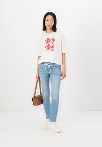 Biela mikina s červenou kvetinovou potlačou, svetlo modré skinny džiny, biele tenisky a hnedá crossbody kabelka. Jednoduchý dizajn a voľný strih.