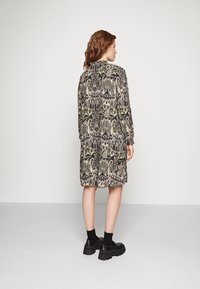 Robe à manches longues dans un motif abstrait noir et vert, avec une coupe décontractée et un ourlet arrondi. Portée avec des chaussures à plateforme noires et des chaussettes.