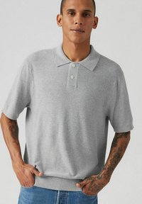 Grå kortärmad polo med krage och treknappsslå. Mjuk textur, elastisk nederkant, ihopparad med blå jeans.