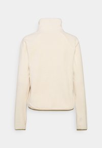 Polarowy pulower w kolorze kremowym z wysokim kołnierzem, raglanowymi rękawami i lekko skróconym dołem. Miękka tekstura z kontrastowymi detalami wykończenia.