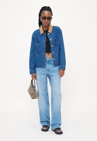 Modrá denimová bunda s hnedým zamatovým golierom, čierny crop top, svetlomodré široké džínsy a kabelka s potlačou zvierat, nosené s čiernymi topánkami.