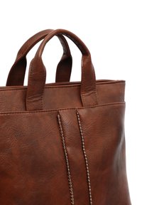 Sac fourre-tout en cuir marron avec double poignée et rangées verticales de perles métalliques sur le devant sur fond blanc.