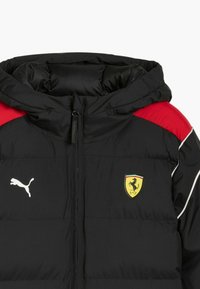 Czarna kurtka puchowa z czerwoną górną częścią, z kapturem, białymi lamówkami i logo Pumy; zawiera emblemat Ferrari na piersi.