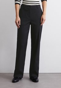 Pantalon noir sur mesure à coupe droite, confectionné dans un tissu lisse. Il est doté d'une fermeture à boutons sur le devant et de poches latérales.