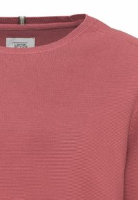 Gros plan d’un pull en maille rose poudré avec un col rond et une étiquette de marque visible à l’intérieur du col.