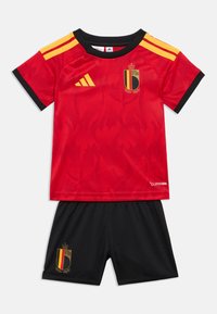 Κόκκινη ποδοσφαιρική φανέλα με σχέδιο φλόγας, που διαθέτει μαύρες λεπτομέρειες, κίτρινες ρίγες και το εθνικό έμβλημα του Βελγίου. Περιλαμβάνονται μαύρο σορτς.