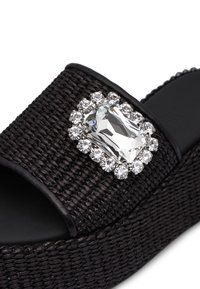 Sandalo platform in tessuto nero con suola piatta, dotato di un grande cristallo rettangolare circondato da piccole pietre brillanti trasparenti.