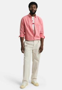 Roze, knoopshirt met een subtiele textuur, witte t-shirt eronder, crèmekleurige broek, witte sneakers met beige accenten.