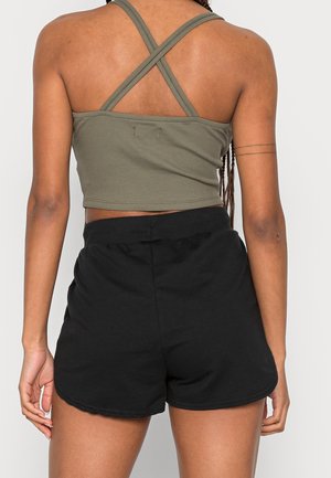 Personne vue de dos portant un crop top vert avec des bretelles croisées et un short noir taille haute sur un fond uni.