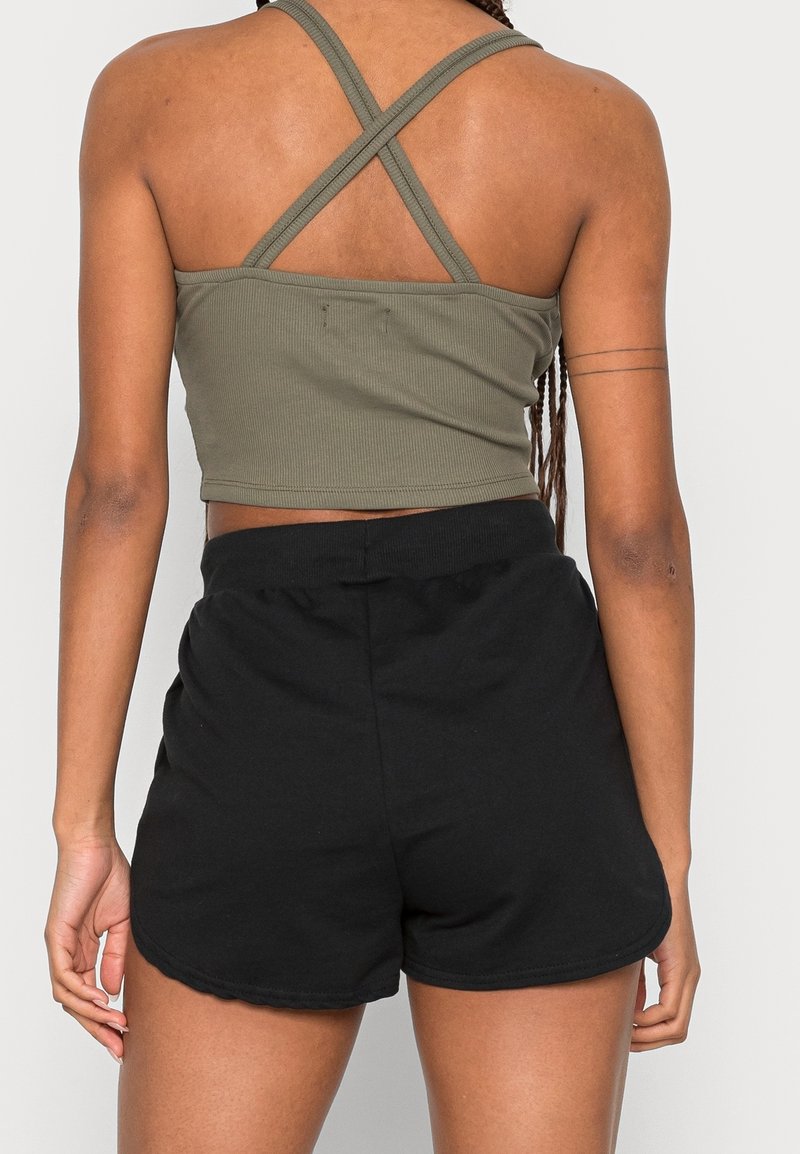 Personne vue de dos portant un crop top vert avec des bretelles croisées et un short noir taille haute sur un fond uni.