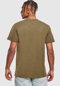 Mørkeolivengrøn kortærmet T-shirt lavet af bomuld. Lige kant og rund hals design, glat struktur, båret med lyseblå jeans.