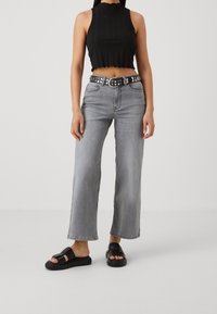 Grå vida jeanstights med hög midja, som bärs med en svart kortärmad ribbad tanktop. Accessoriserad med ett nitar-bälte i svart och svarta sandaler.
