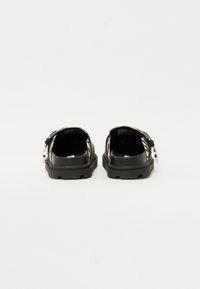 Black sandals with a textured upper featuring a white and black pattern, adjustable strap, and a thick rubber sole.