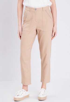 Beige hoge taillebroeken met voorzakken, een gestructureerde stof en zilveren ritsaccenten, gecombineerd met witte sneakers op een effen achtergrond.