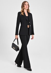 Blazer nero su misura con bottoni dorati, pantaloni a sbuffo abbinati e tacchi a punta neri. Portando una borsa nera a texture coccodrillo.