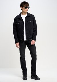 Sort denimjakke med knaplukning og lommer, parret med en hvid t-shirt og sorte jeans. Sorte sneakers fuldender outfittet.