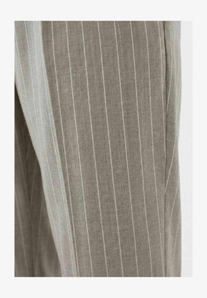 Nærbilde av grå bukser i stoff med tynne hvite vertikale nålestriper og detalj ved sidesømmen.