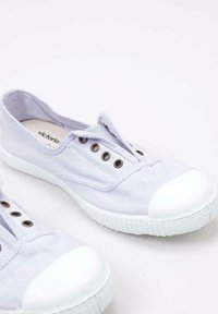 Scarpe slip-on in tela di lavanda chiaro con punta e suola in gomma bianca, dotate di tre occhielli in metallo e una superficie superiore texturizzata.