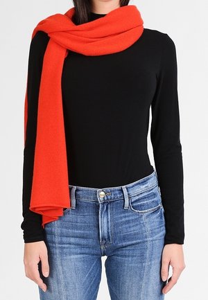 Écharpe rouge en tissu doux, drapée autour du cou, associée à un haut noir à manches longues et un jean bleu, mettant en valeur le contraste de couleurs et la texture.