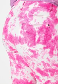 Jeans de unicolor rosa con un corte de cintura alta y bolsillos traseros, presentando una mezcla de blanco y varias tonalidades de rosa en un patrón irregular.