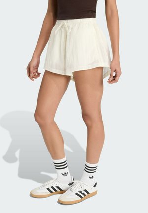 Witte, lichtgewicht korte broek met een elastische tailleband en trekkoord. Gecombineerd met witte en zwarte sneakers en gestreepte sokken.