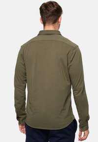 Olive green long-sleeve shirt made of smooth fabric, featuring a collar, button cuffs, and a rounded hem. No visible patterns or accents.