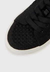 Pantof sport negru cu un design geometric texturat pe partea superioară, cu șireturi negre și talpă de cauciuc albă.