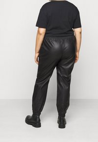 Czarne skórzane spodnie dresowe z elastycznym paskiem w talii i mankietami, zestawione z czarną koszulką z krótkim rękawem. Gładka tekstura, swobodny krój.