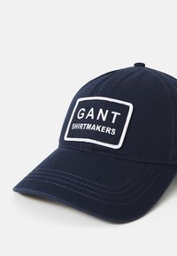 Temno modra bejzbolska kapa iz bombaža, z vezenim pravokotnim obližem z belim napisom "GANT SHIRTMAKERS".