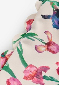 Fabric with scalloped edge featuring a floral print of pink and purple flowers with green stems on a light beige background.