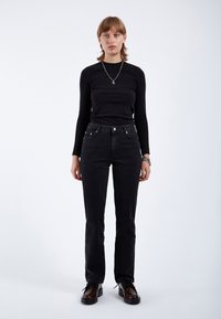 Maglietta nera a maniche lunghe abbinata a jeans neri a vita alta. L'outfit presenta un design elegante, hardware minimale e una texture liscia e opaca.