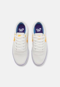 Bílé plátěné tenisky s oranžovým logem Nike, fialovými a modrými stélkami a bílými tkaničkami. Zaoblený design špičky s texturovaným povrchem.