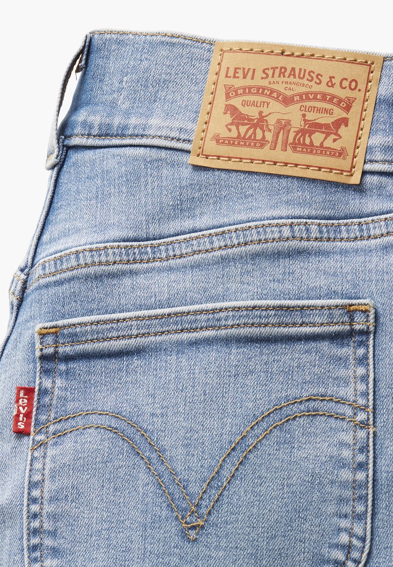 Jean en denim bleu clair avec une patch en cuir ornée de graphismes rouges et marron, poches arrière emblématiques avec des coutures courbées et une étiquette Levi's.