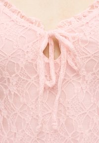 Κοντινό πλάνο ροζ δαντελένιου υφάσματος με δεμένη φιόγκο στη λαιμόκοψη και λεπτό ανθικό μοτίβο.